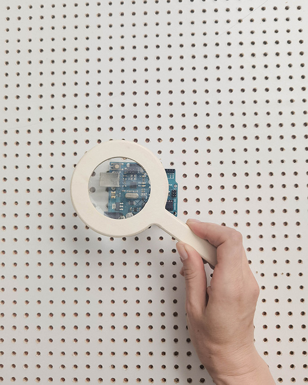 Hand holding magnifying glass over circuit board on pegboard, representing exploring how computers work